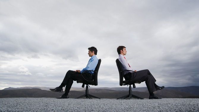 屋外に置かれたチェアに背中合わせで座る2人の男性