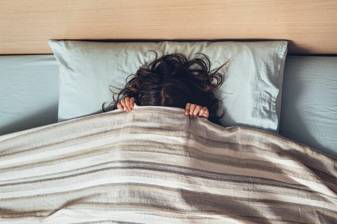 ベッドシーツで顔を覆う小さな女の子