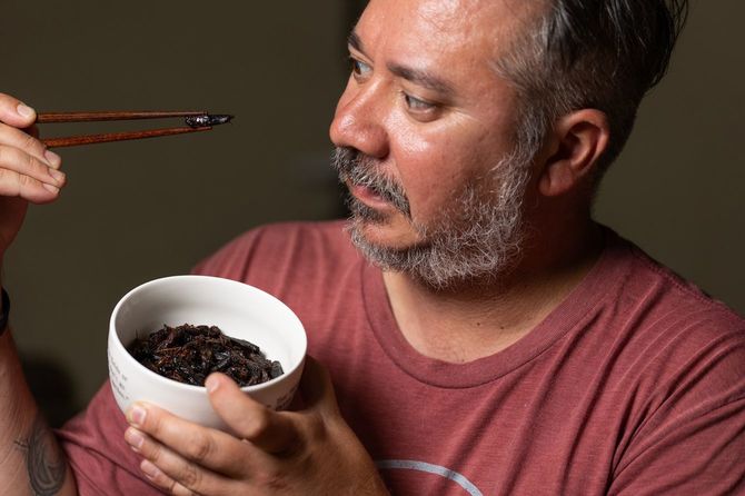 イナゴの佃煮を箸につまみ見つめる男性