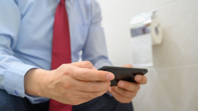 便座に座ってスマホを使用する男性