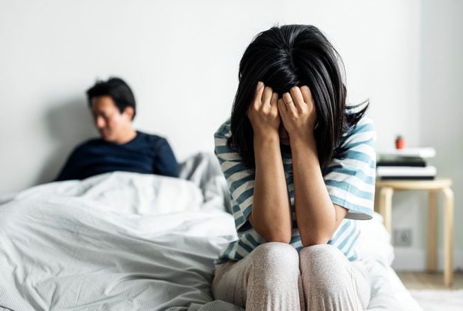 頭を抱える妻と、ベッドに座る夫