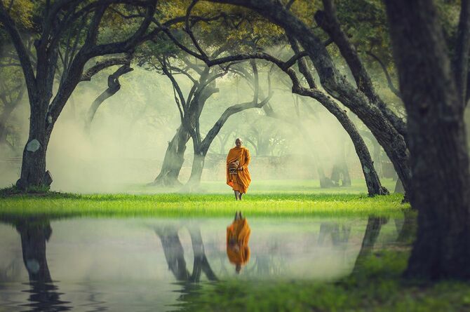 湖、仏教と深い森の反射で僧侶のハイキング