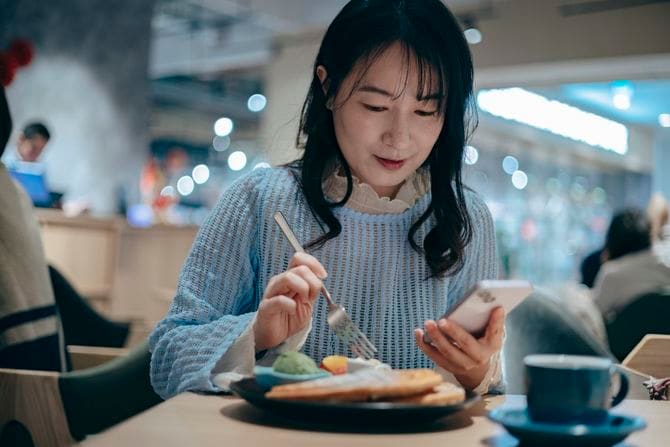 女性がレストランで食事を楽しみながらスマートフォンを使っている