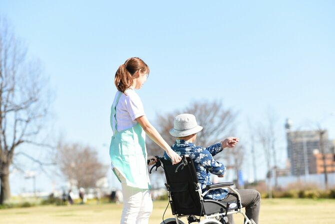 青空の下、車椅子に乗ったシニア男性と介護士
