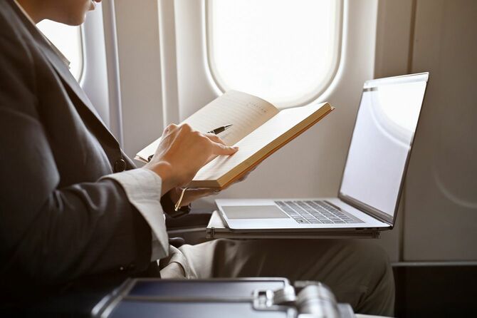 飛行機に乗りながら、ノートに何かをチェックしたり書いたりしているビジネスマン