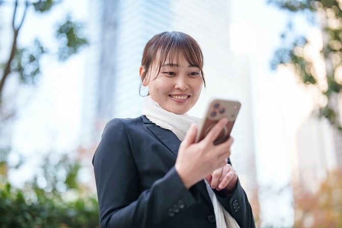 街でスマートフォンをチェックしながら微笑む日本のビジネスウーマン