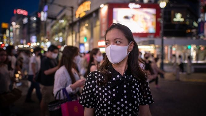 夜のスクランブル交差点を歩くマスクを着用した若い女性