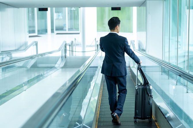 スーツケースを手にエスカレーターを進んでいるビジネスパーソン