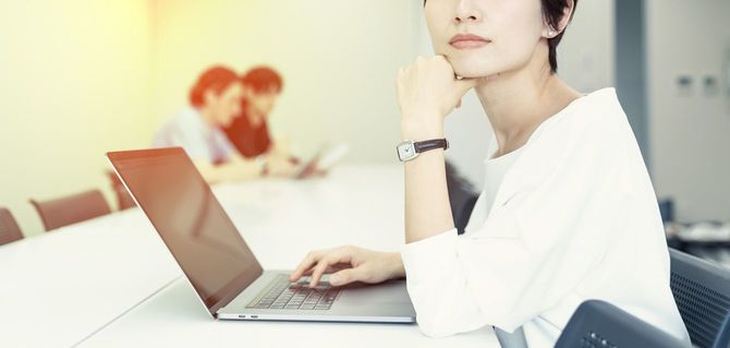 ノートパソコンから目を離し、あごに手をやりこちらを向いているビジネスウーマン