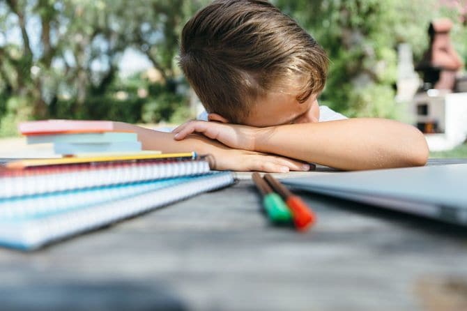 教科書やノートが置かれた机の上に突っ伏している男の子