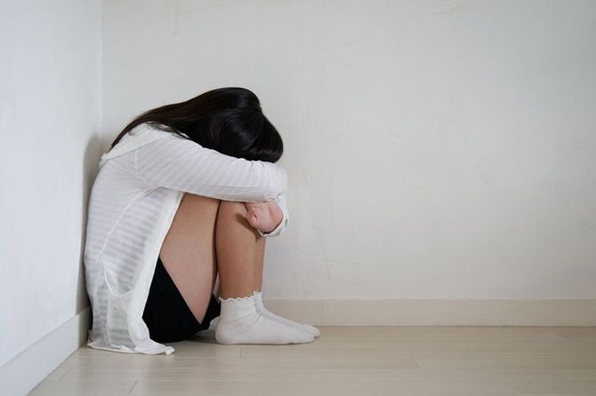 床に膝を抱えて座り、顔をうずめる子供