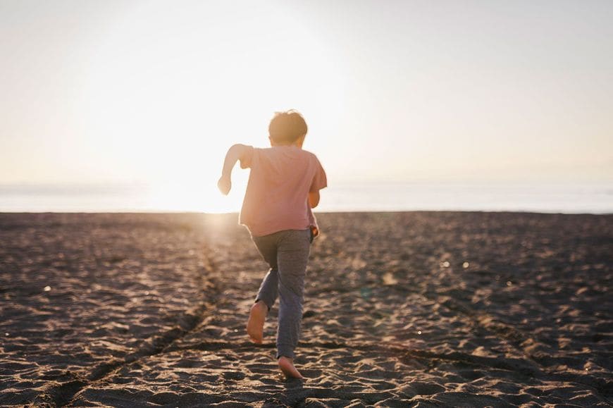 夕暮れ時のビーチを走る少年