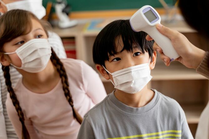 教室で並ぶ子供たちを非接触体温計で体温を計っていく教師の手元