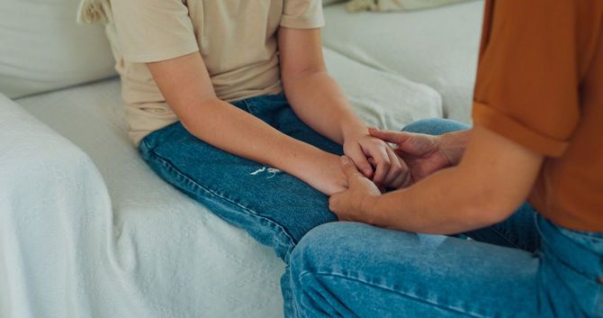 ソファーに座った息子と目線を合わせ、手を握りながら話しかけている親