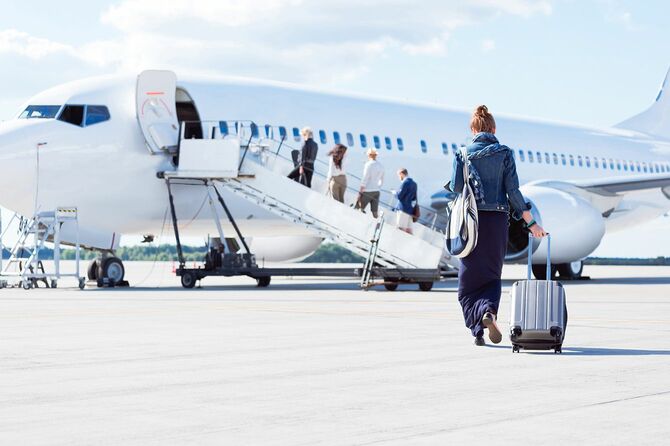 飛行機に向かって歩く荷物を持つ若い女性の背面図。休暇に行く女性旅行者