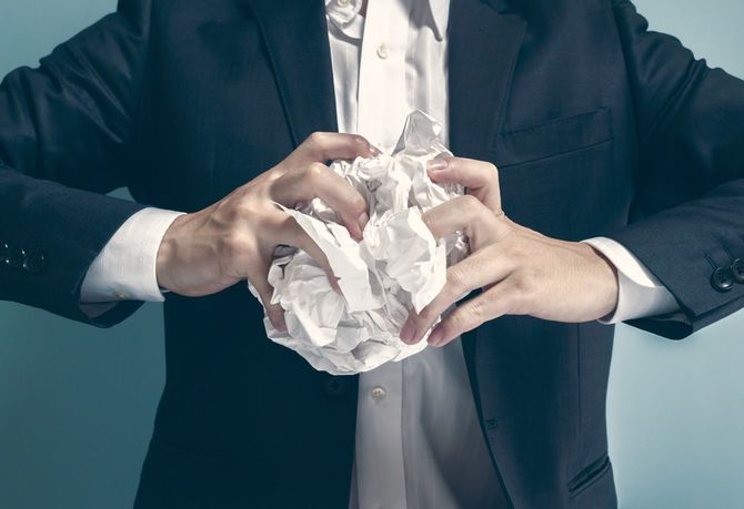 紙を両手で丸めるビジネスマン