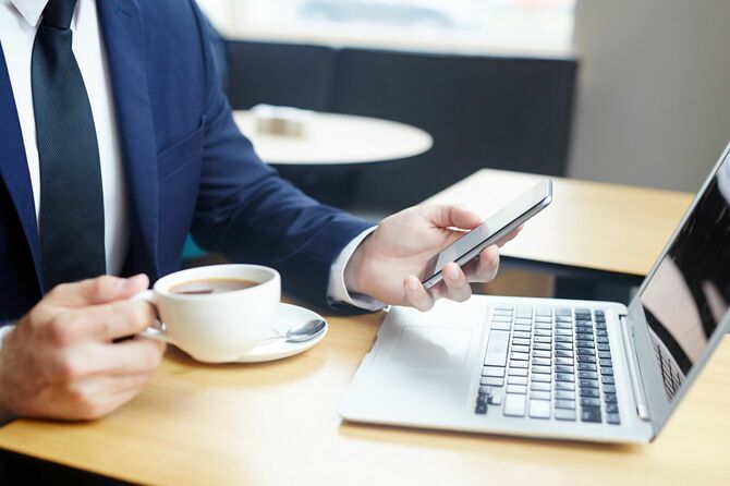 コーヒーを飲むエレガントなビジネスマンの手にスマートフォン