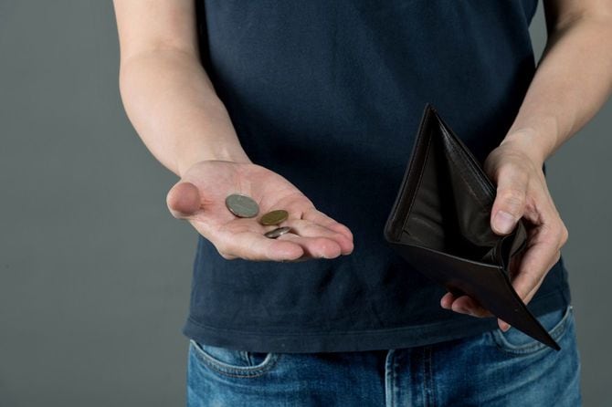空の財布と少しの硬貨を手に持つ男性