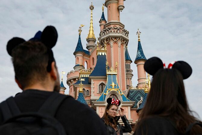 ディズニーランド・パリの『眠れる森の美女』の城と、ミッキーマウスとミニーマウスの耳をつけた来園者