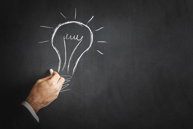 黒板にチョークで、電球の絵を描いている手元