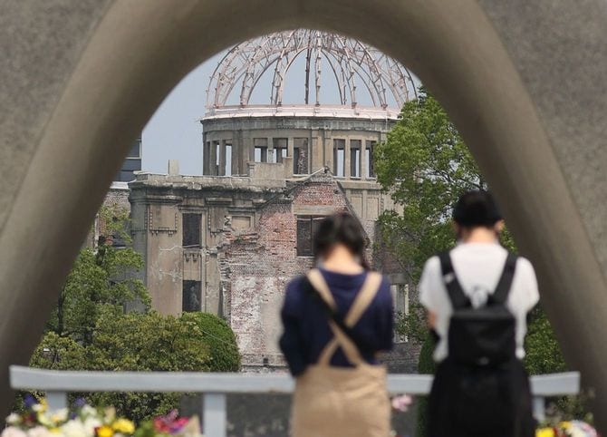 原爆が投下されて75年となる「原爆の日」を前に、原爆死没者慰霊碑に手を合わせる人たち。奥は原爆ドーム＝2020年8月5日午前、広島市中区