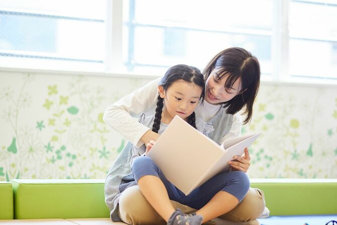 保育園で子どもたちと一緒に絵本を見ている女性教師