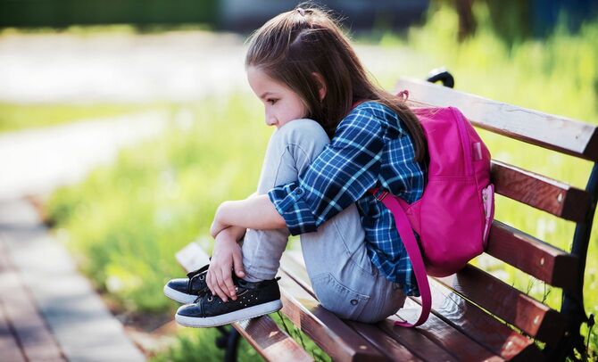 公園のベンチで悲しげな表情で膝を抱えて座っている少女