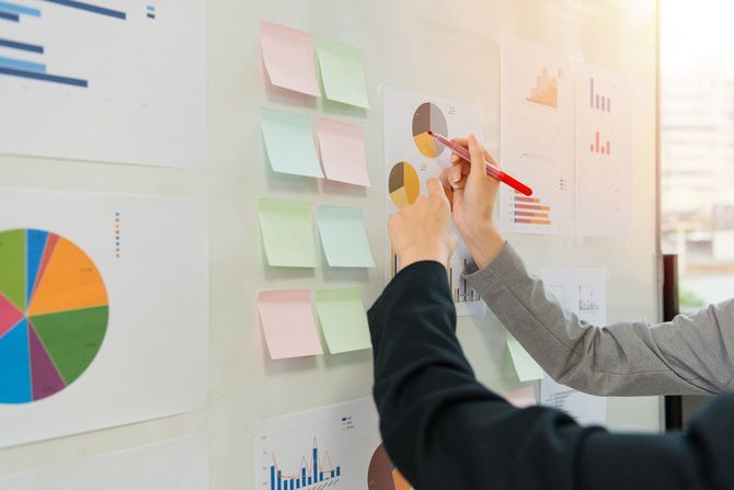 ホワイトボードに貼った円グラフに赤を入れようとする女性の手元