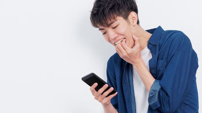 メールの内容に、驚きのあまり無自覚に手を噛んでしまう青年