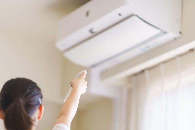 エアコンのリモコンでスイッチを入れる女性