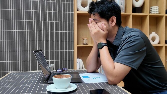 男性がラップトップとコーヒーカップを持ってテーブルに座っています