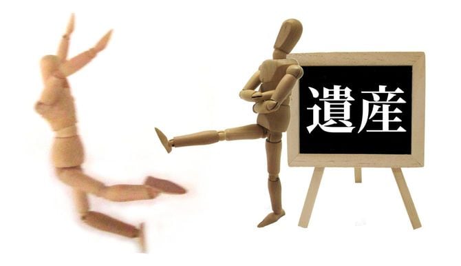 遺産と書かれたボードの前から人形を蹴り出すもう1体の人形
