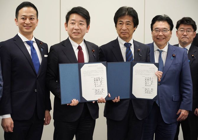 社会保障制度改革の骨子で合意し、署名した文書を手にする自民党の田村憲久元厚生労働相(中央)と日本維新の会の梅村聡氏(左から2人目)=2026年7月7日、国会内