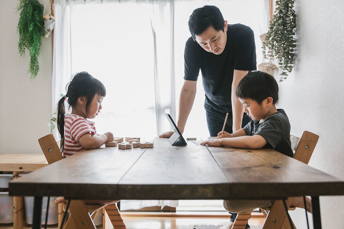 アジアの父親は、自宅でEラーニングコースを受講している子供たちを見ています。