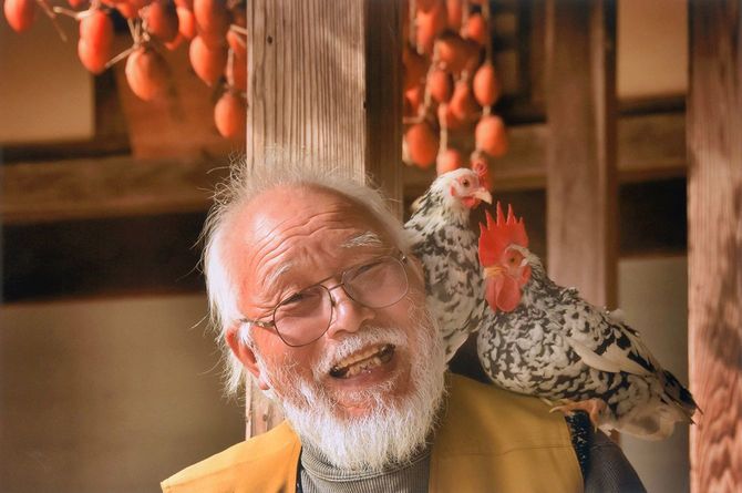 鶏を肩に乗せて笑う老年男性