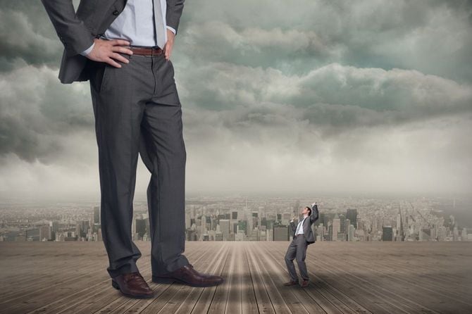 手を腰に当てた巨大なビジネスマンの足元にいる驚く小さなビジネスマン