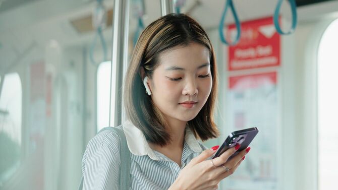 電車の中でイヤホンを使用して音楽を聞く女性