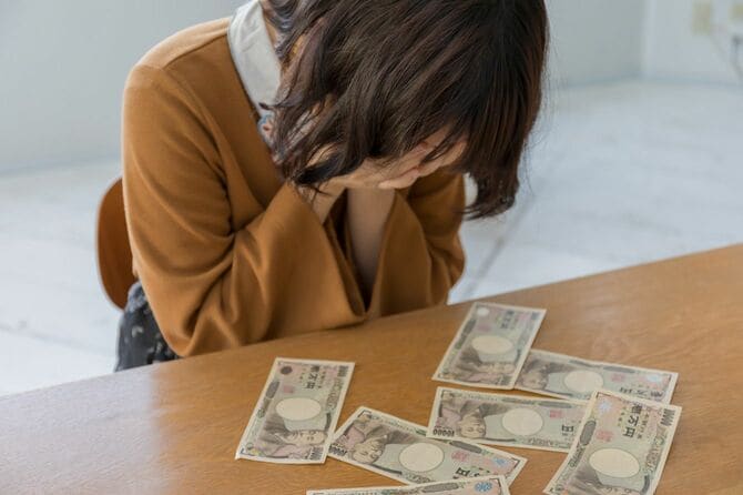 お金を前にして顔に手を当てて悲しむ女性