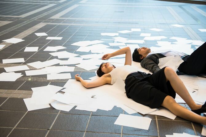紙の散らばった床に寝る人