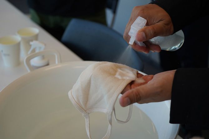 マスクにスプレーをかけている茂木康之氏の手元