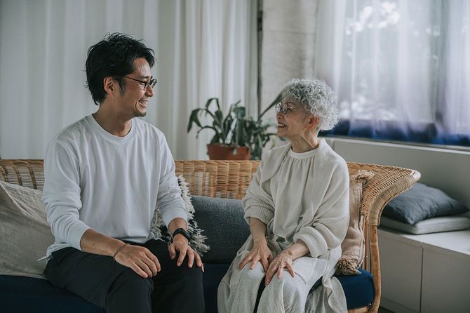 ソファに座って笑顔で話す男性と高齢の母親