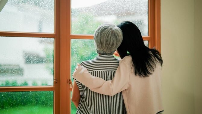 家の窓際で寄り添う女性と彼女の母親