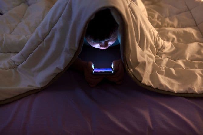 布団の下で携帯電話を見る少年