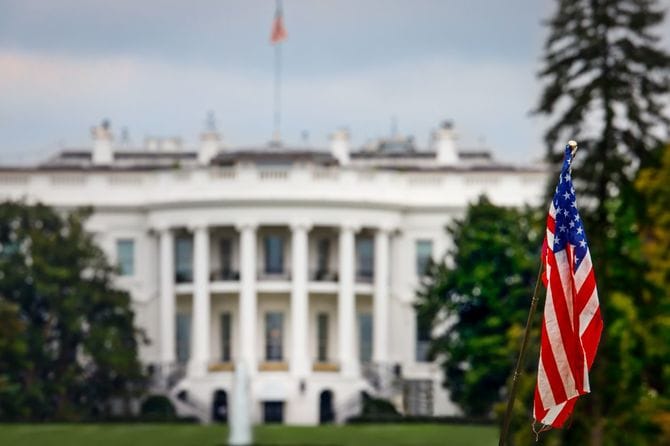 ワシントンDCのホワイトハウスの前に立つ観光客のアメリカ国旗