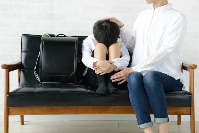 ソファの上で膝を抱えて泣いている小学生の男の子を励ます母親