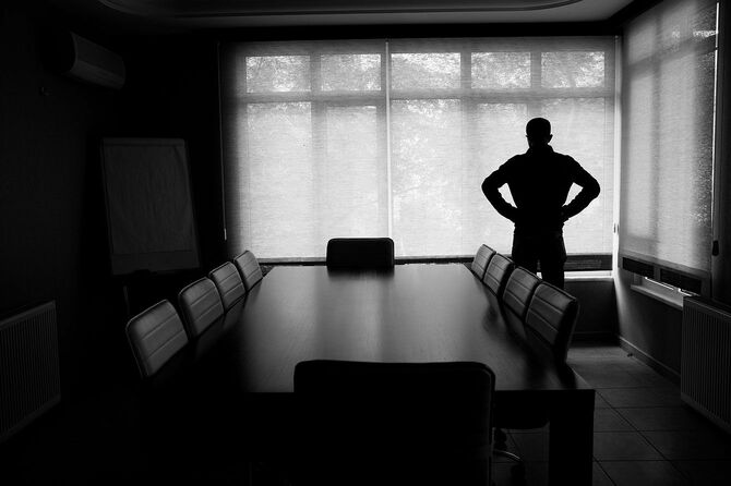 暗いオフィスの会議室に一人で立っているビジネスマンのシルエット