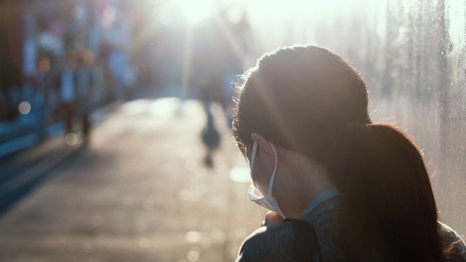 明るい日差しのなかにいる、マスクを着用した女性