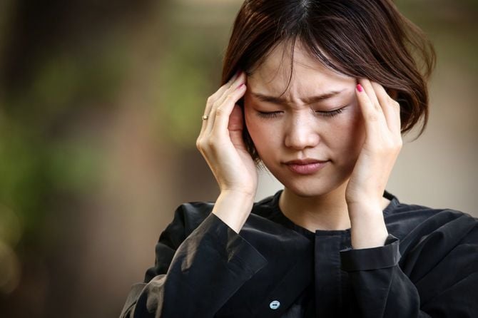 頭痛に思わずこめかみに指をあてる女性