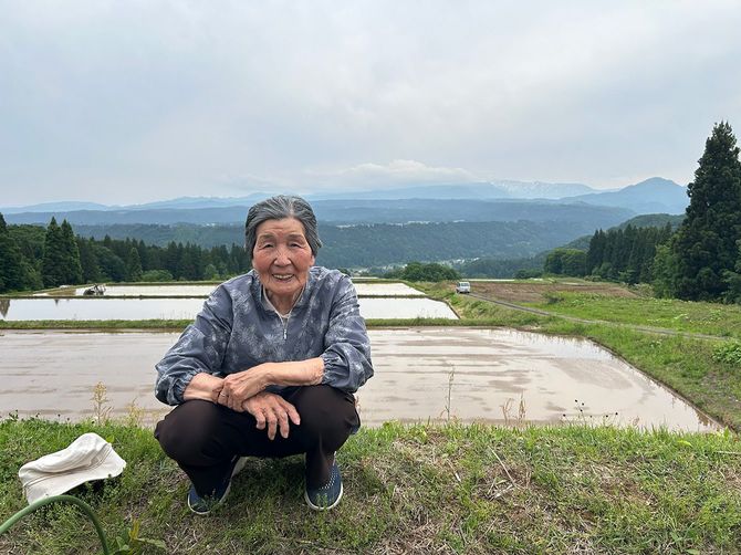 かつて「よそ者の嫁」たち仲間7人で作った山の上の田んぼを背景に微笑む桑原千恵さん