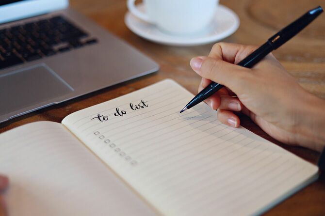 ペンを持つ手、オフィスの机の上のノート、ラップトップ、コーヒーカップ